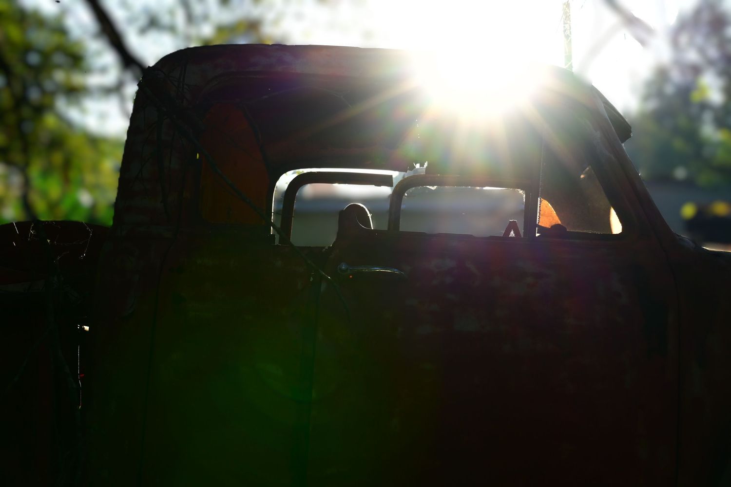 The sun rises over the roof of a rusted out antique pickup truck.