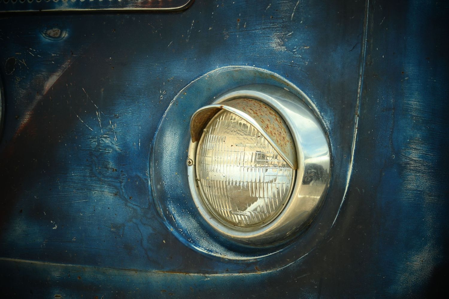 A close-up of the headlight of a old, weathered blue VW van.