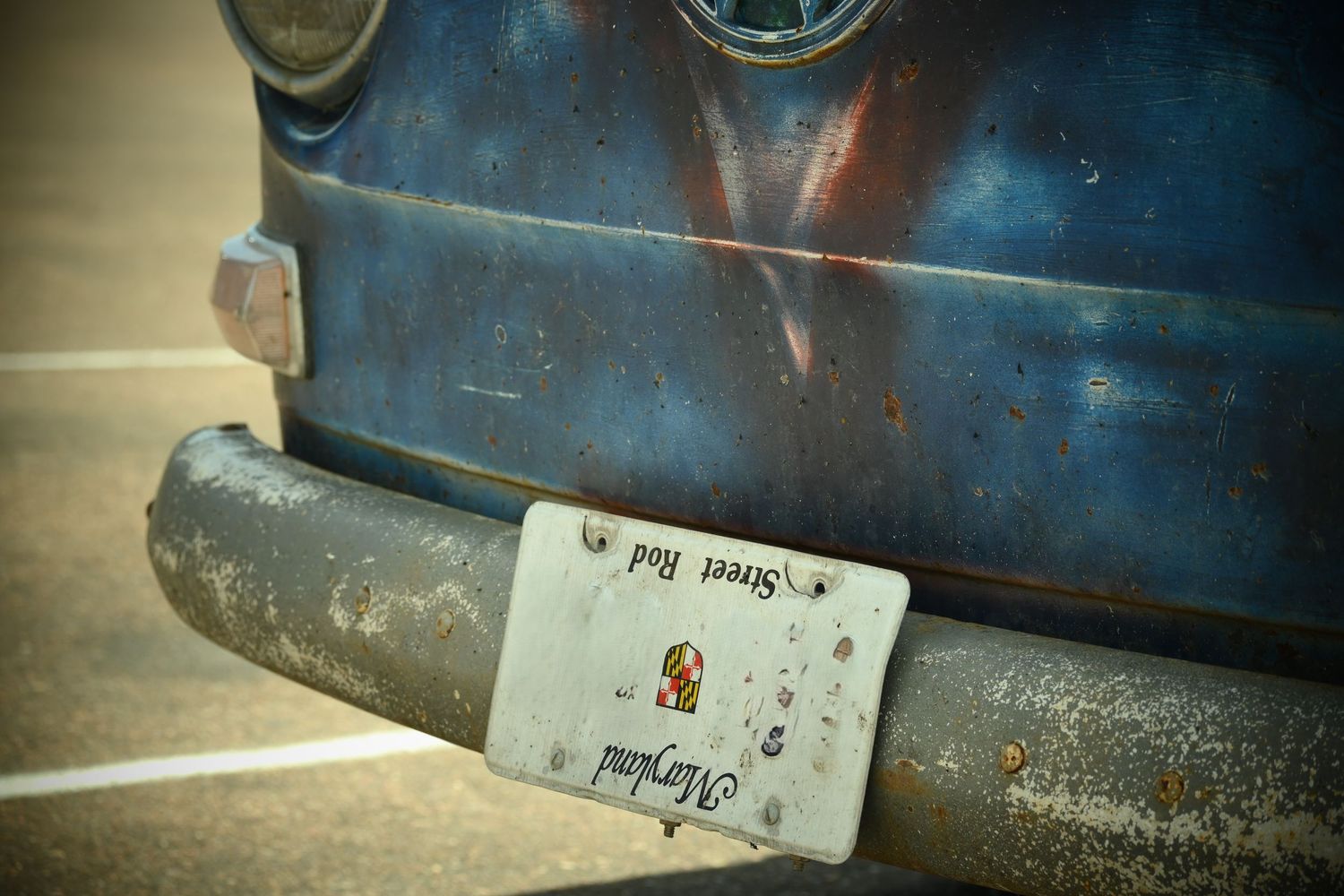 The bumper of an old, weathered blue VW van with an upside down Maryland license plate.