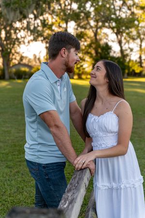 A couple in casual attire shares a romantic moment outdoors during golden hour in a grassy field.