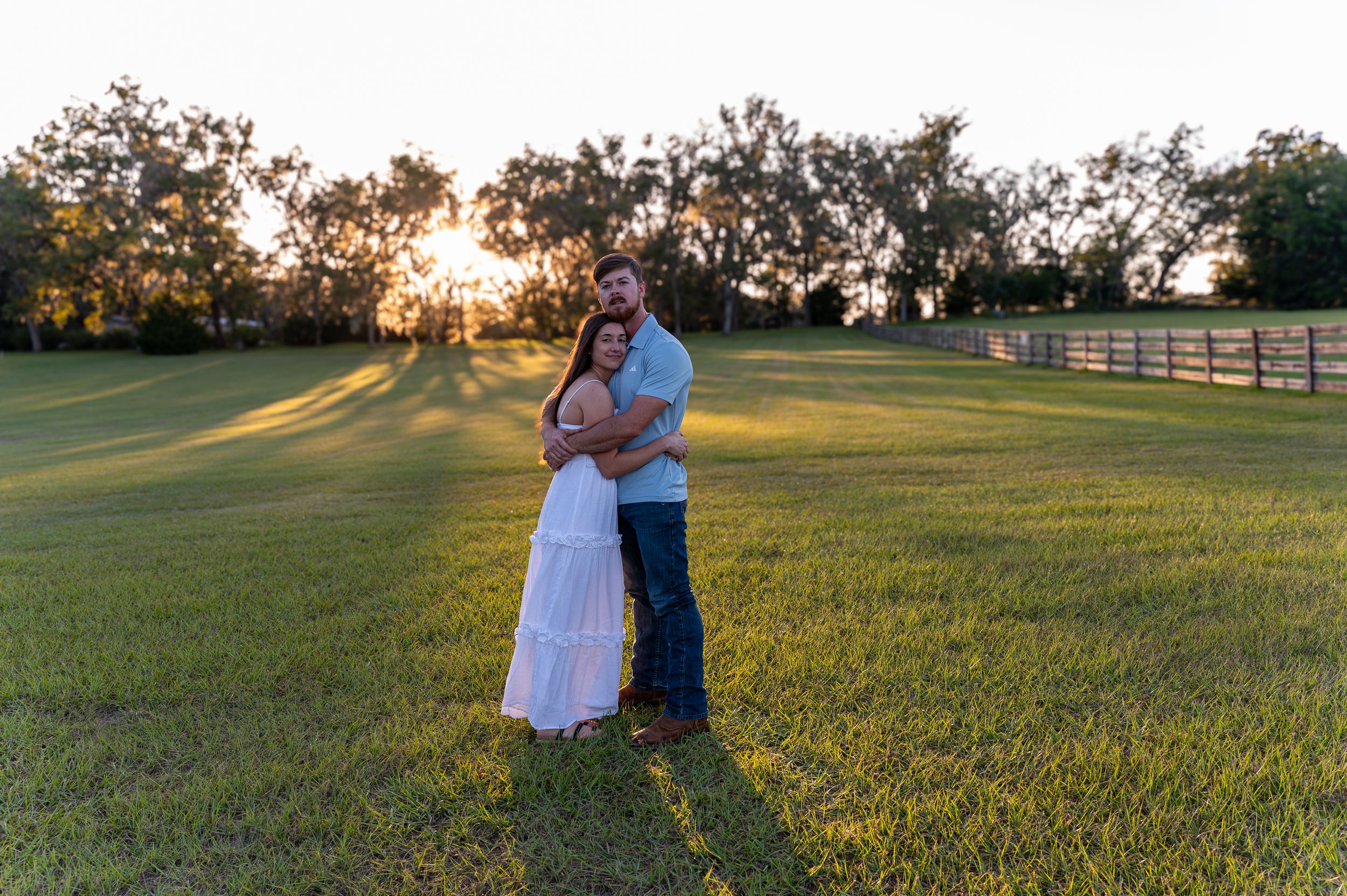 A couple embraces in a golden sunlit field during a romantic sunset photo session.