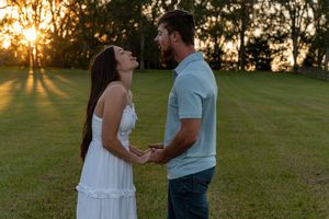 A couple shares an intimate moment in a grassy field during golden hour sunset.