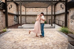 Couple dancing together on a brick courtyard under an elegant pergola with string lights at an outdoor venue.