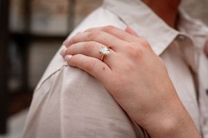 Close-up of a diamond solitaire engagement ring on a woman's finger resting on a shoulder.