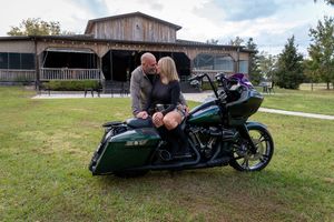 A custom dark green motorcycle is parked on the grass in front of a rustic wooden building.