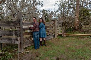 Couple standing by rustic wooden fence in countryside with Spanish moss trees.