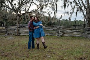 Couple embracing near split-rail fence surrounded by Spanish moss-draped trees.