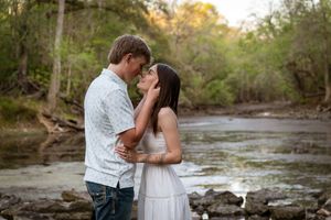 Couple sharing a romantic moment by a rocky creek surrounded by lush green trees during an outdoor engagement photo session.