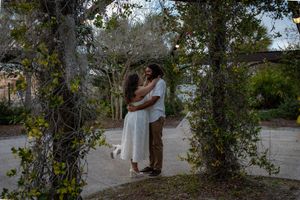 A couple shares a romantic kiss under a vine-covered archway in a lush garden at dusk.