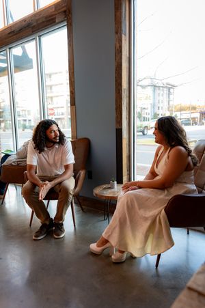 Two people having a conversation in a modern cafe with large windows and natural light.