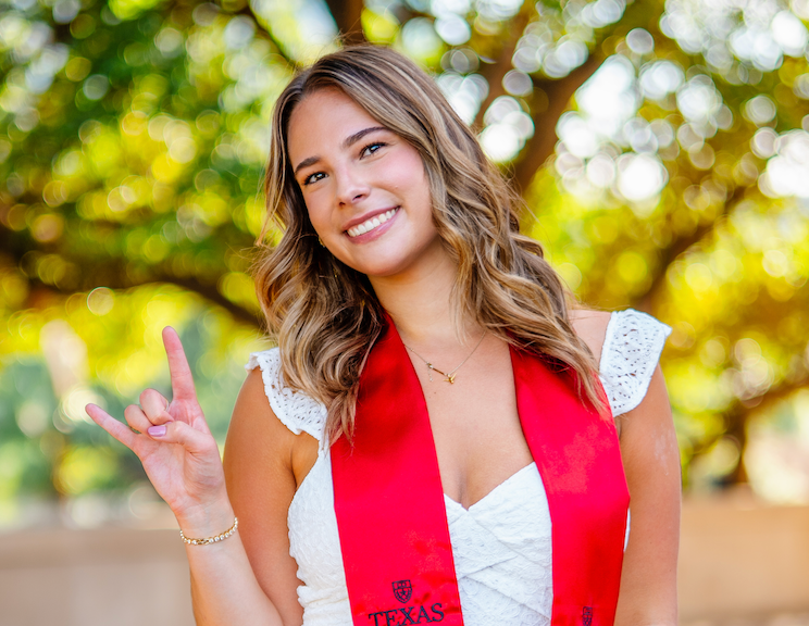 A person in a red vest and white dress poses outdoors in a sunny garden setting with natural lighting.