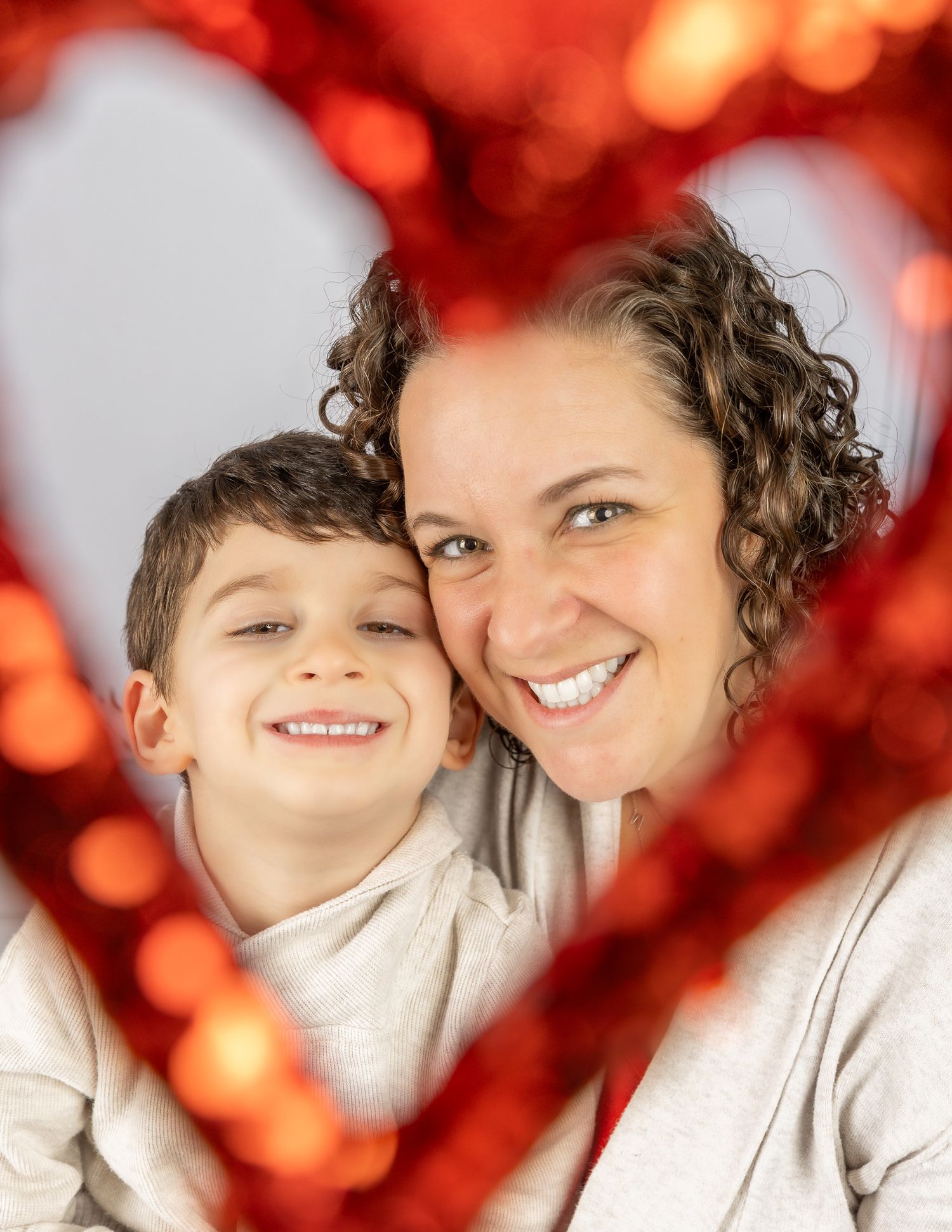 A parent and child pose together against a festive red bokeh background with warm holiday lighting.