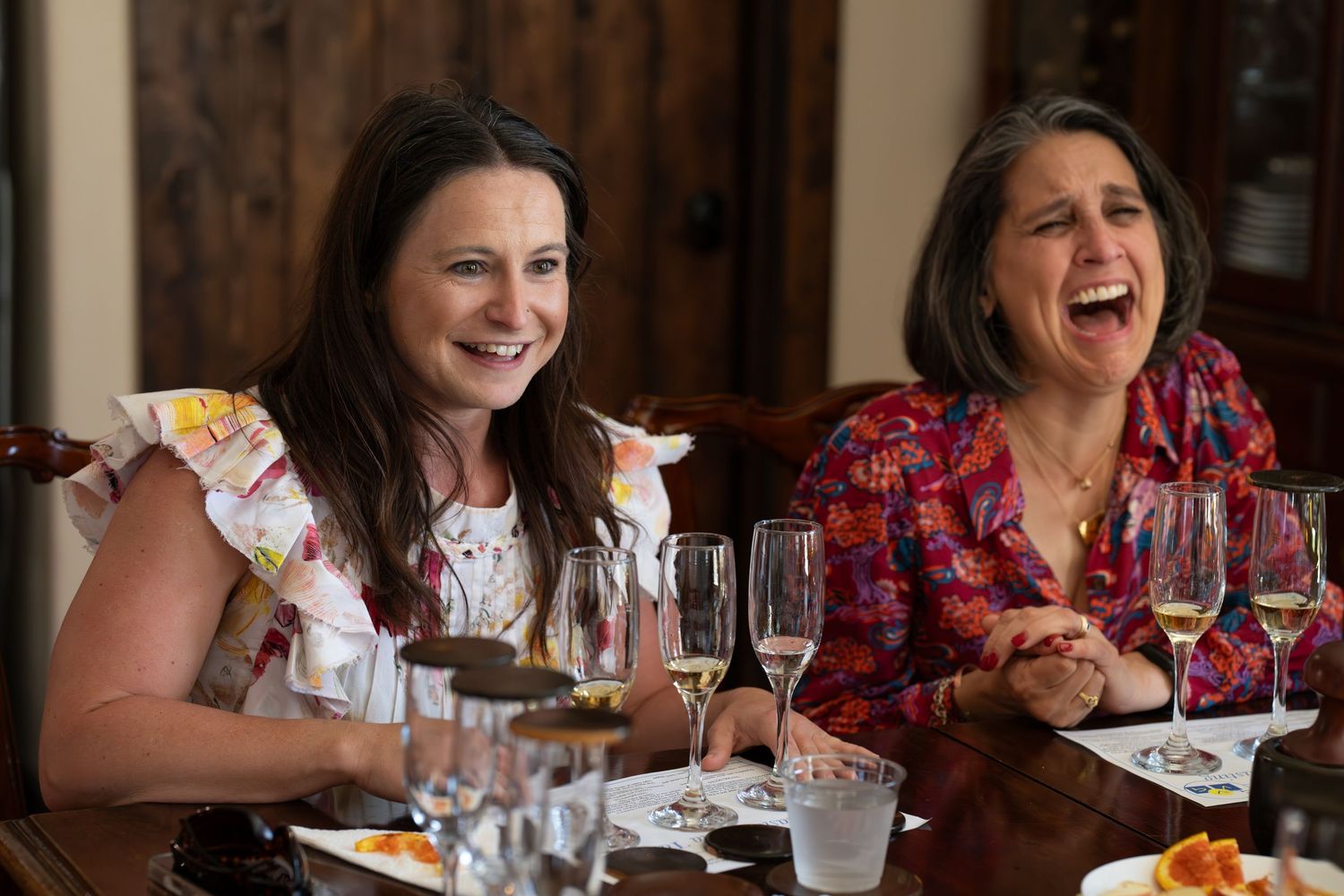 Two women laughing and enjoying wine tasting at a dining table with wine glasses.