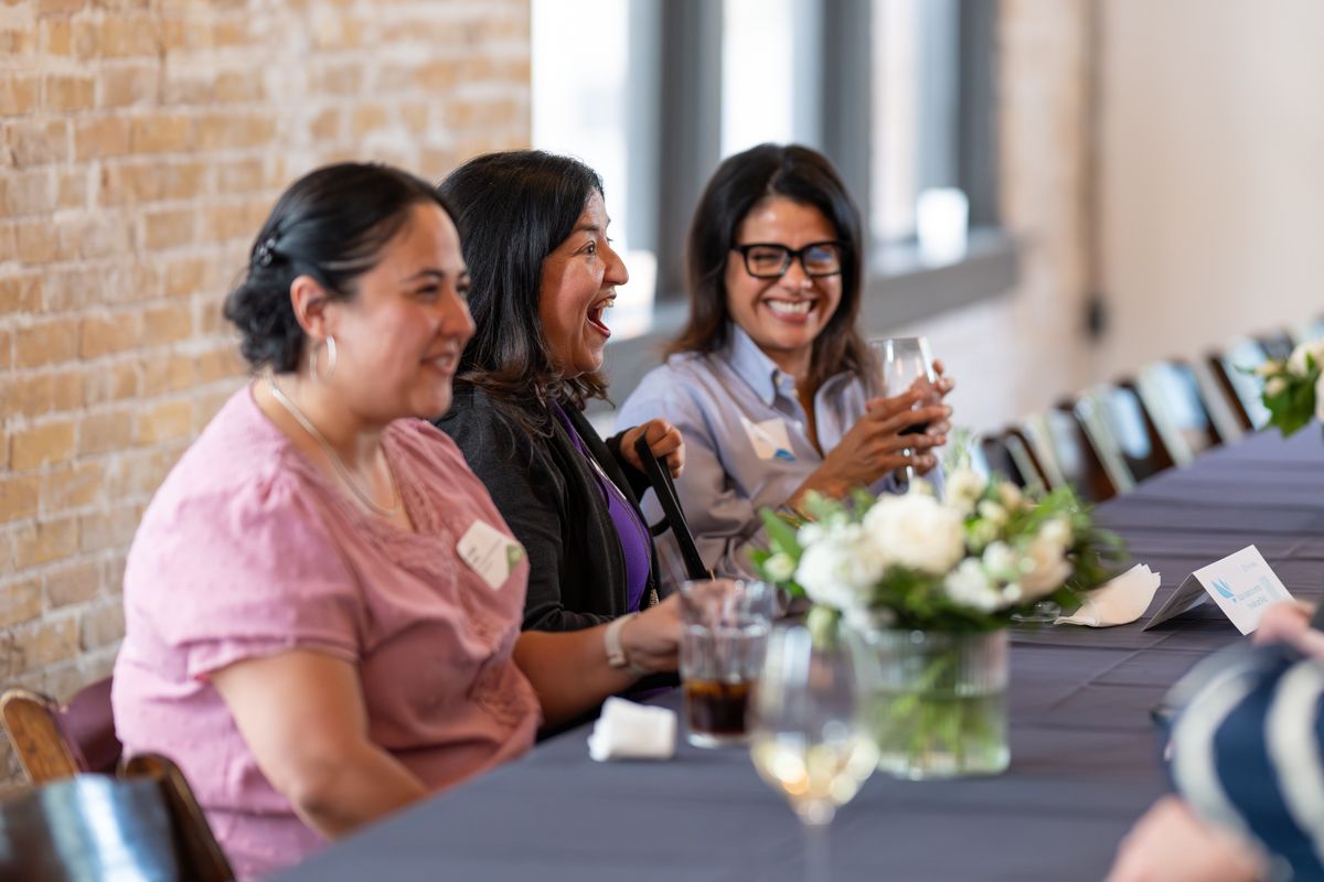 A group of people gather around a table for a social event with brick walls in the background.