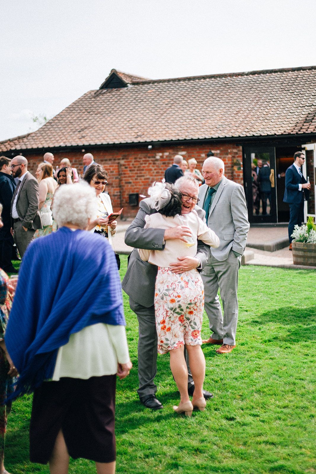 Crondon Park Wedding guests gather on a grassy lawn outside a rustic brick barn venue during a daytime celebration.
