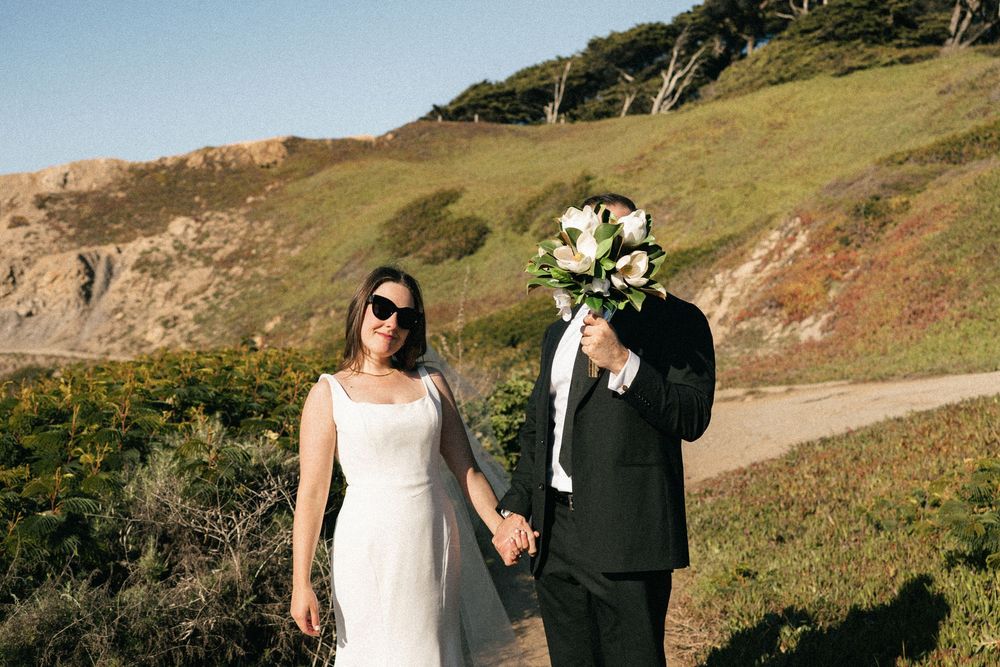 A wedding couple poses together against a scenic coastal hillside backdrop on a sunny day in San Francisco.