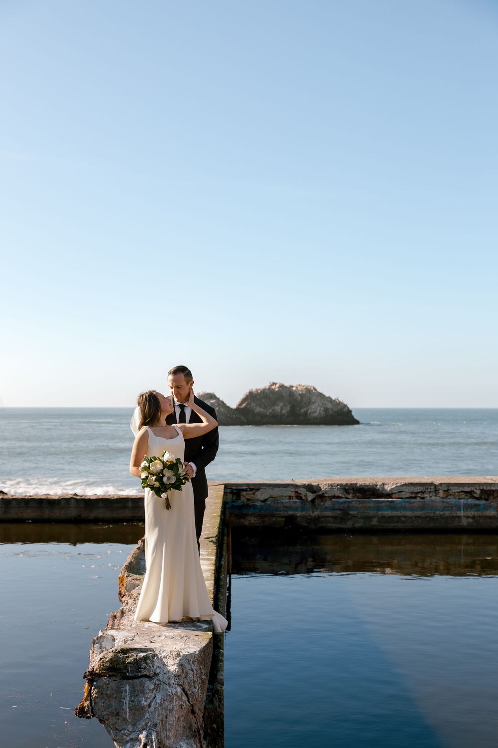 Couple shares romantic moments by the ocean on rocky coastal cliffs during their wedding photoshoot at Sutro Baths.