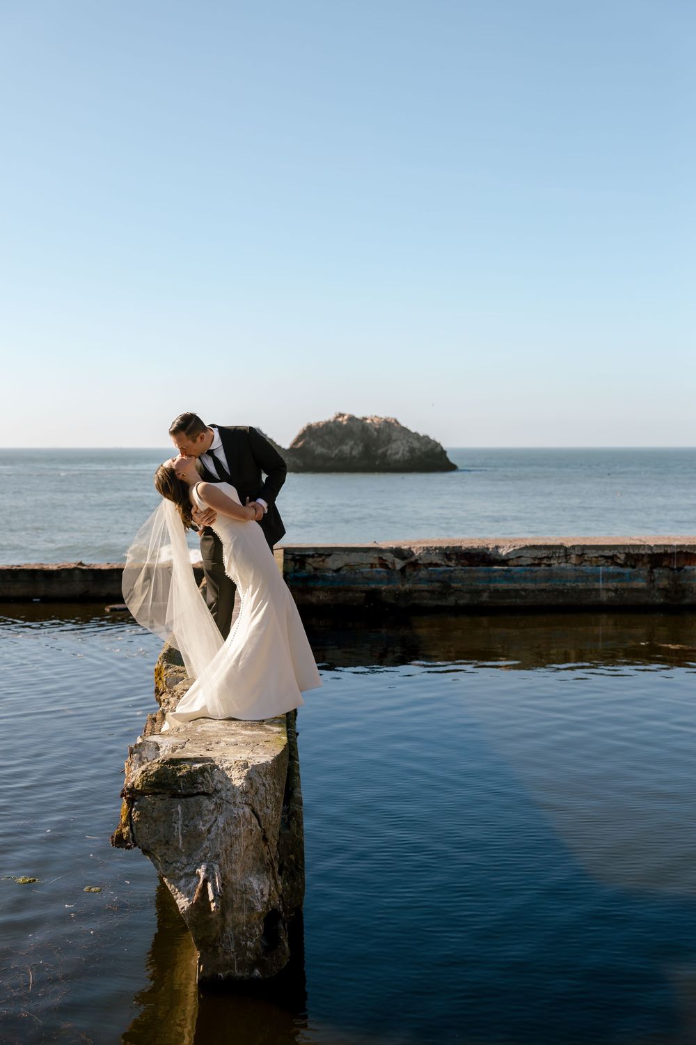 A couple shares a romantic moment at Sutro Baths in San Francisco with the Pacific Ocean and rocky coastline in view.