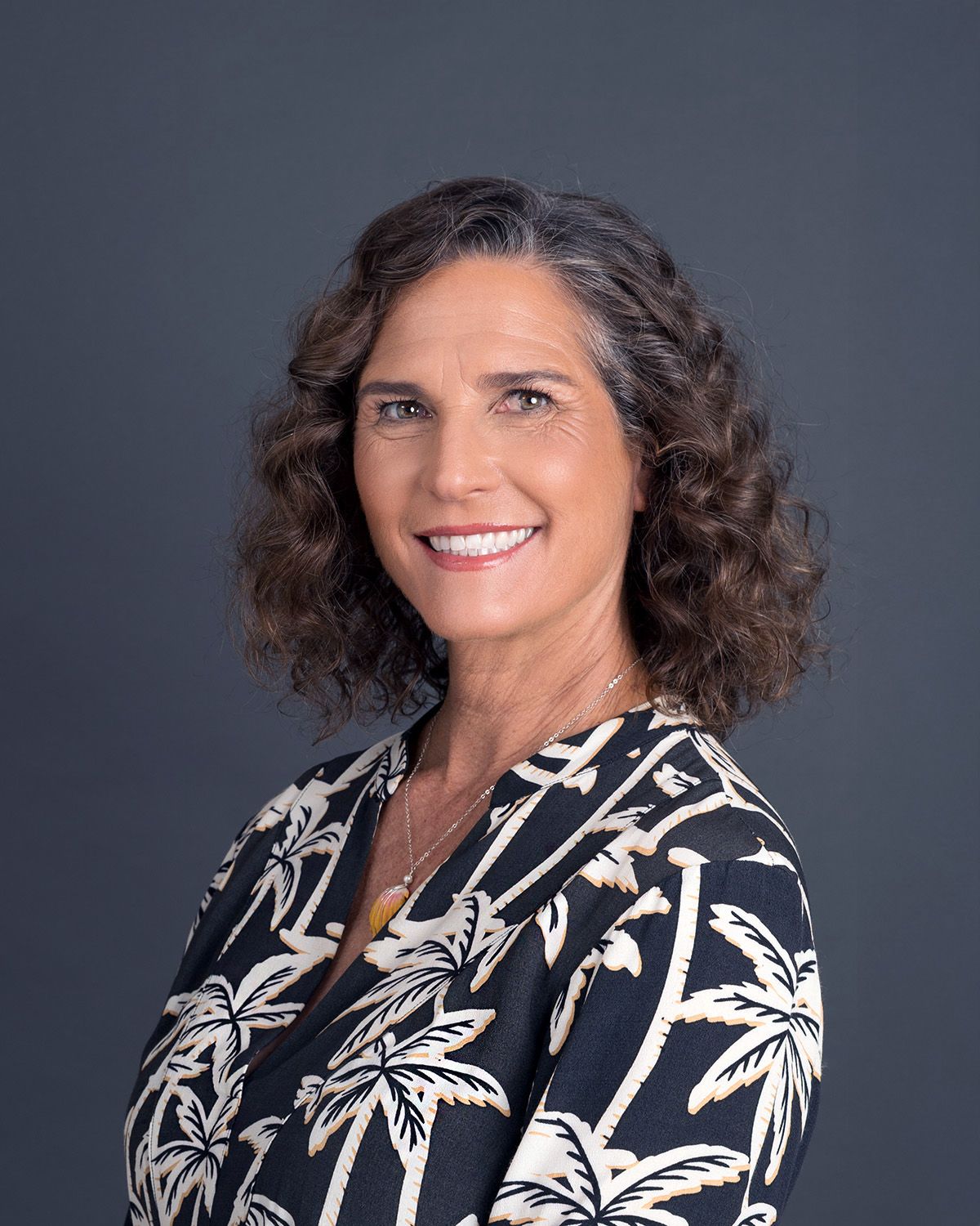 A woman in a black and white floral print blazer poses in a series of professional headshots against a dark background.
