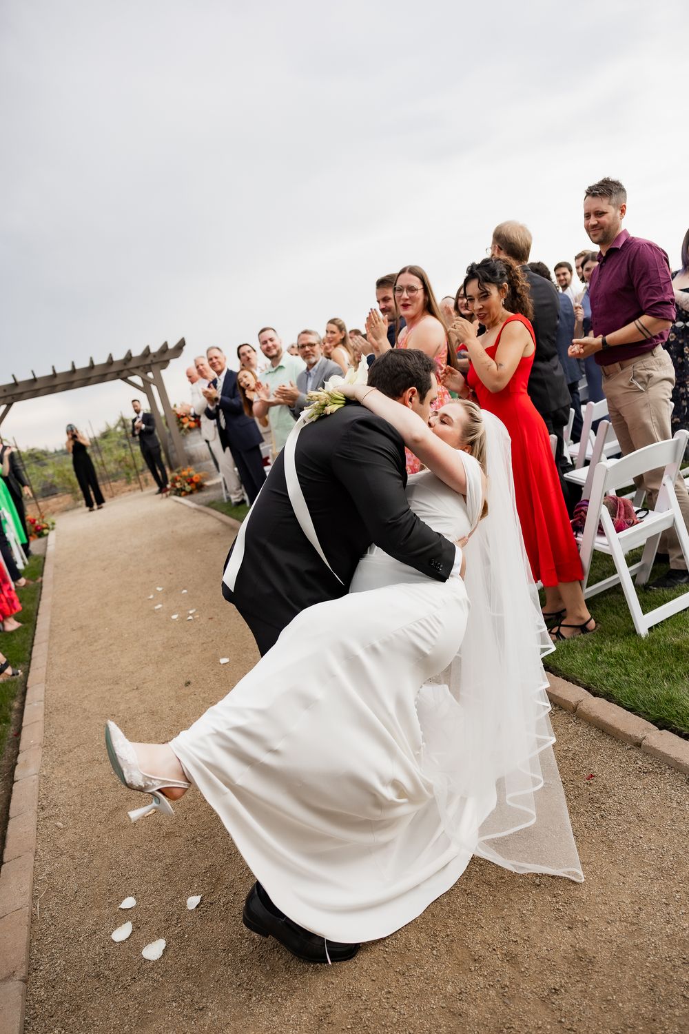 Wedding couple performs a dramatic dip during their first dance as guests watch from the outdoor ceremony venue.