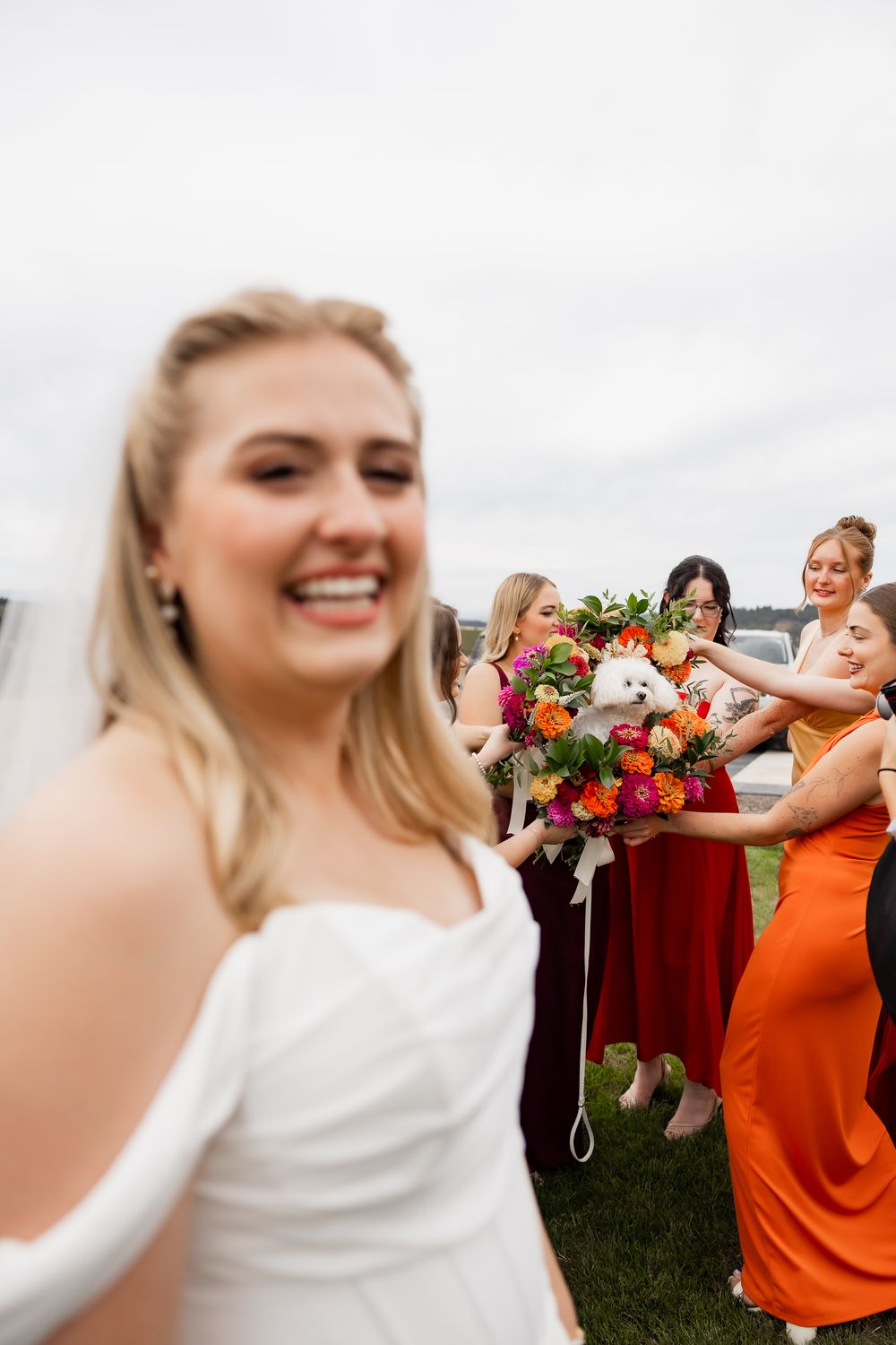 Wedding party wearing orange and burgundy dresses pose together outdoors for celebratory photos.