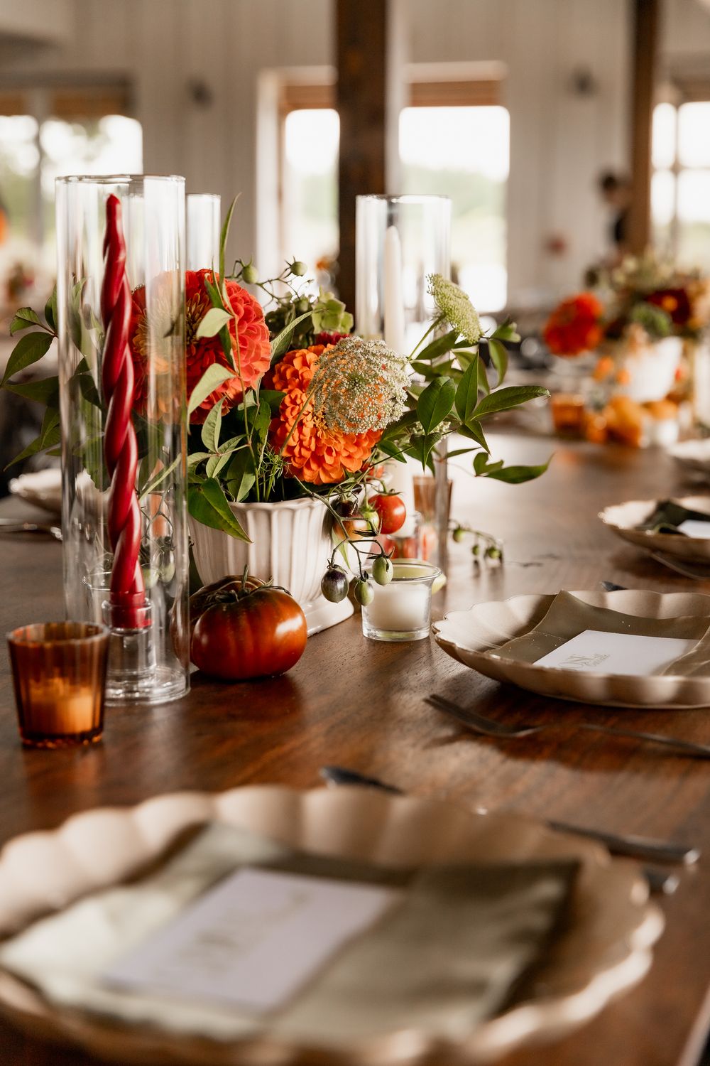 Elegant table setting with copper vases, red taper candles, and tropical greenery on a dark wooden dining table.