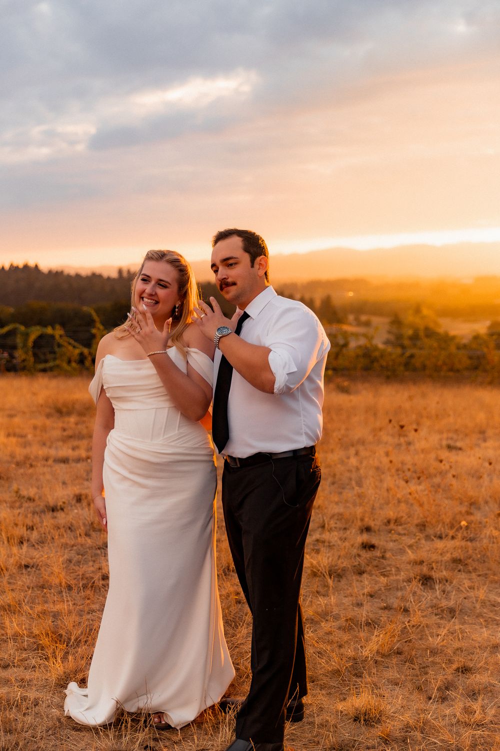 A couple shares an intimate moment during sunset in a golden field with warm lighting and mountains in background.