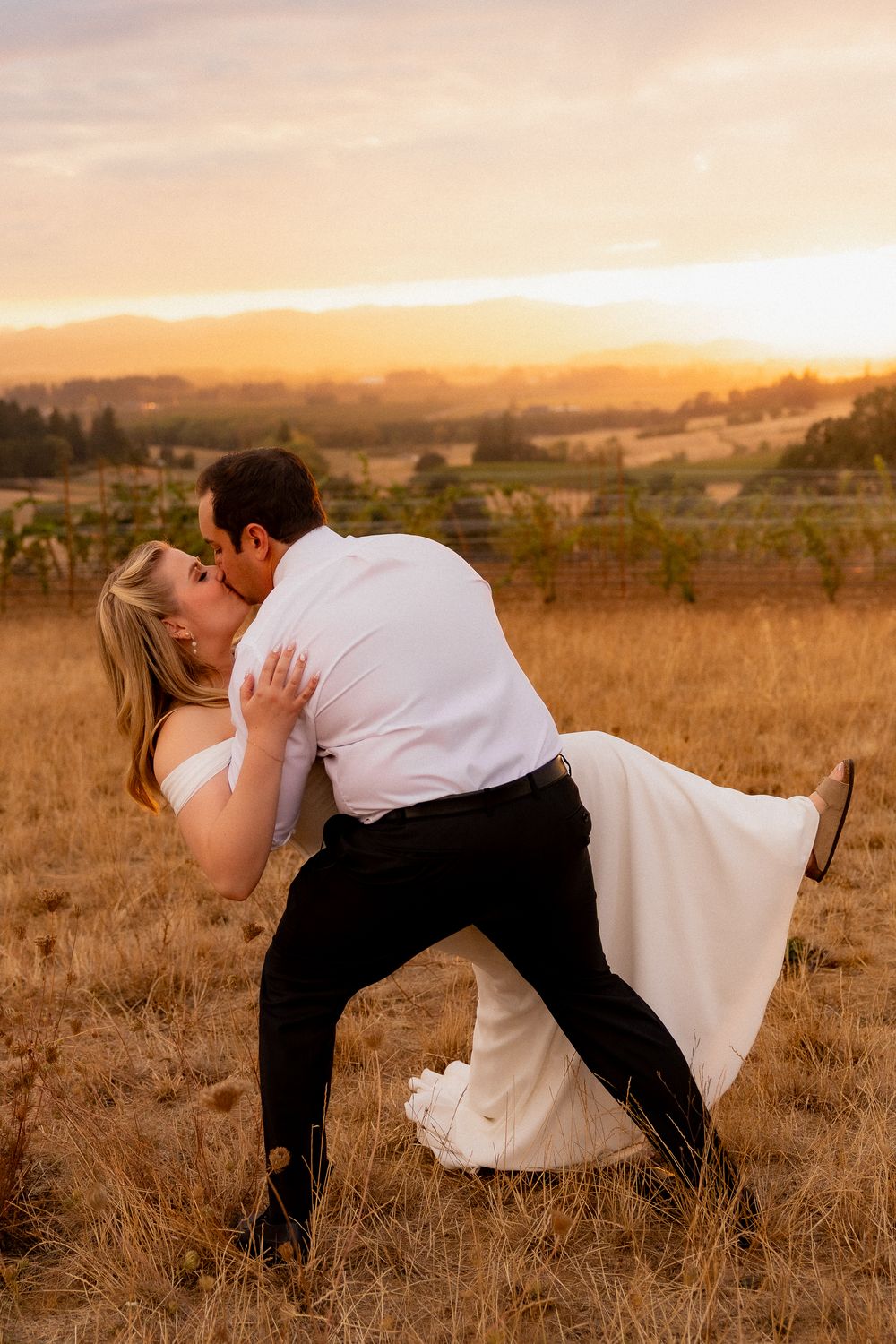 A romantic dip pose between newlyweds in a sun-drenched field.