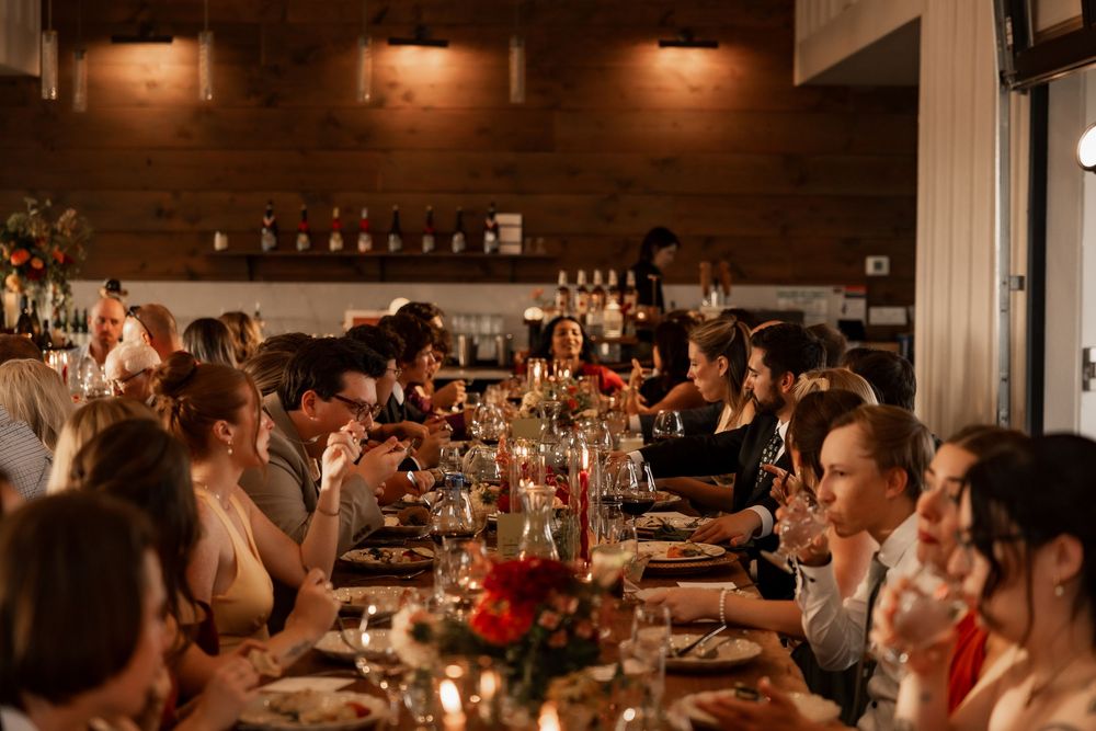 Long wooden tables set for a wedding reception with moody lighting and rustic decor in a restaurant setting.