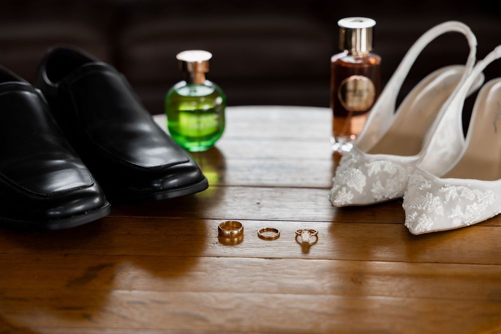 Wedding accessories including rings, shoes, perfume bottles and other bridal details arranged on wooden surface.