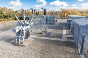 Electrical substation equipment and transformers arranged in rows at an industrial power facility on a sunny day.