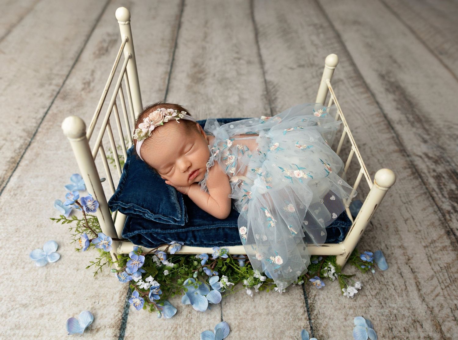 Tilton NH newborn photography of a sleeping baby girl in a blue tulle dress, fine art studio portrait with soft florals and vintage bed.