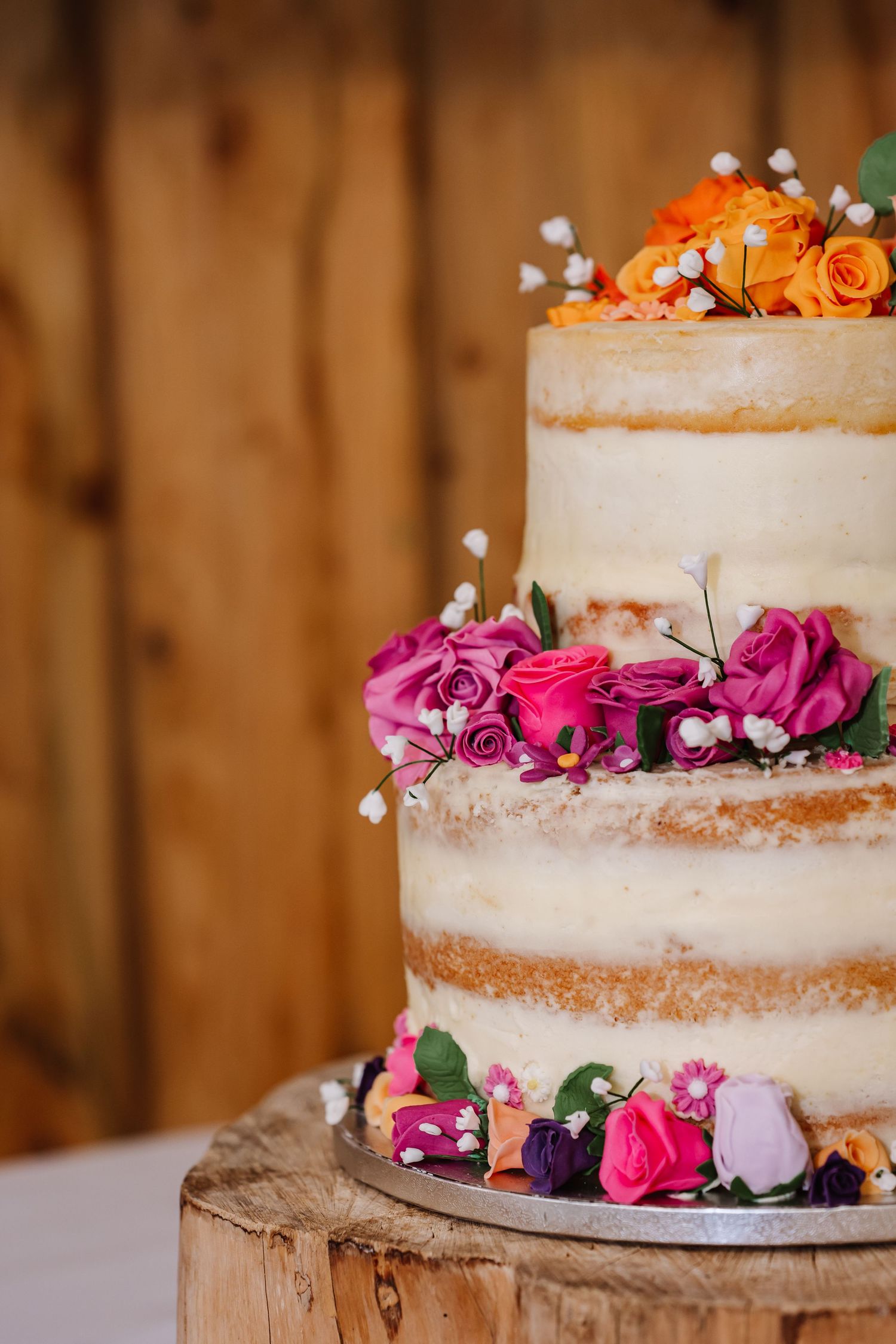 Naked wedding cake with pink and orange roses at Waterside Country Barn and Mill, Taunton. Somerset candid wedding photographer