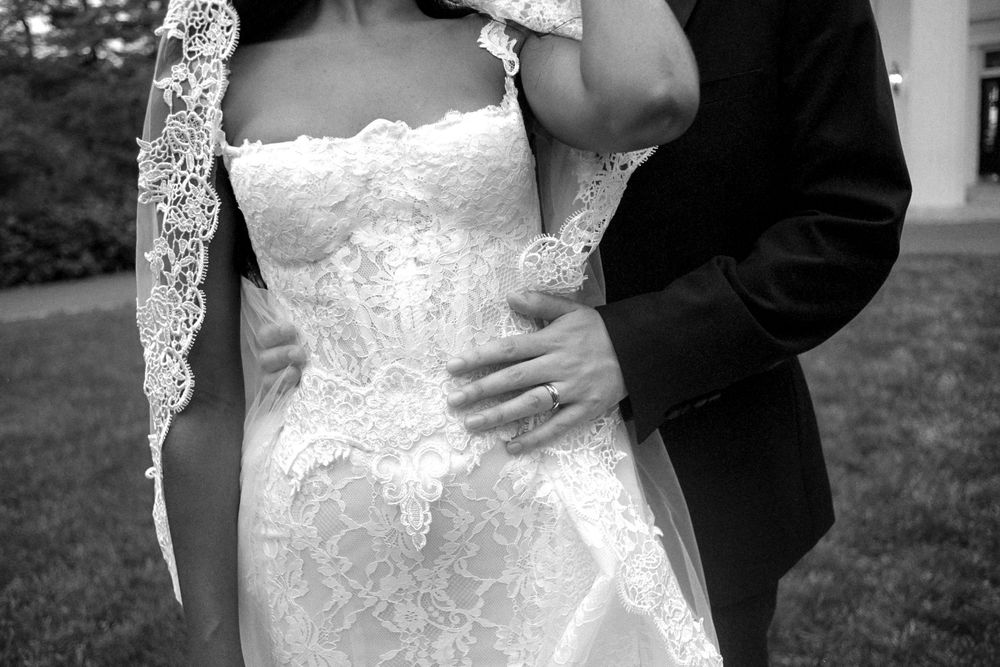 A close-up black and white photo showing the intricate lace details of a wedding dress and suit.