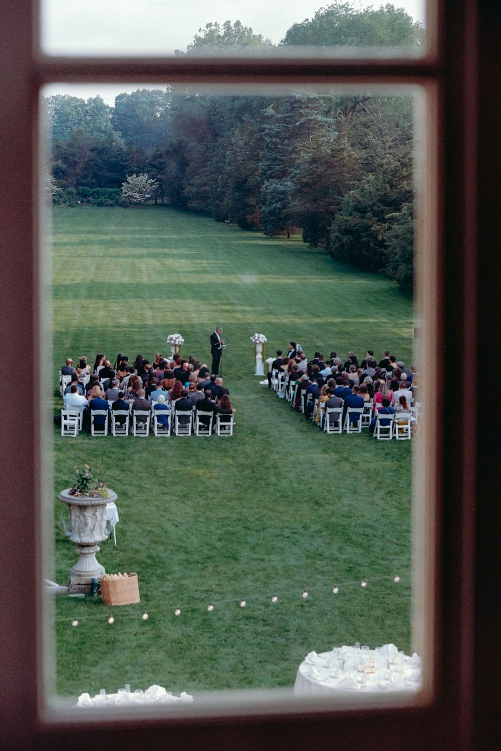 Outdoor wedding ceremony setup with white chairs arranged in rows on a green lawn surrounded by trees.