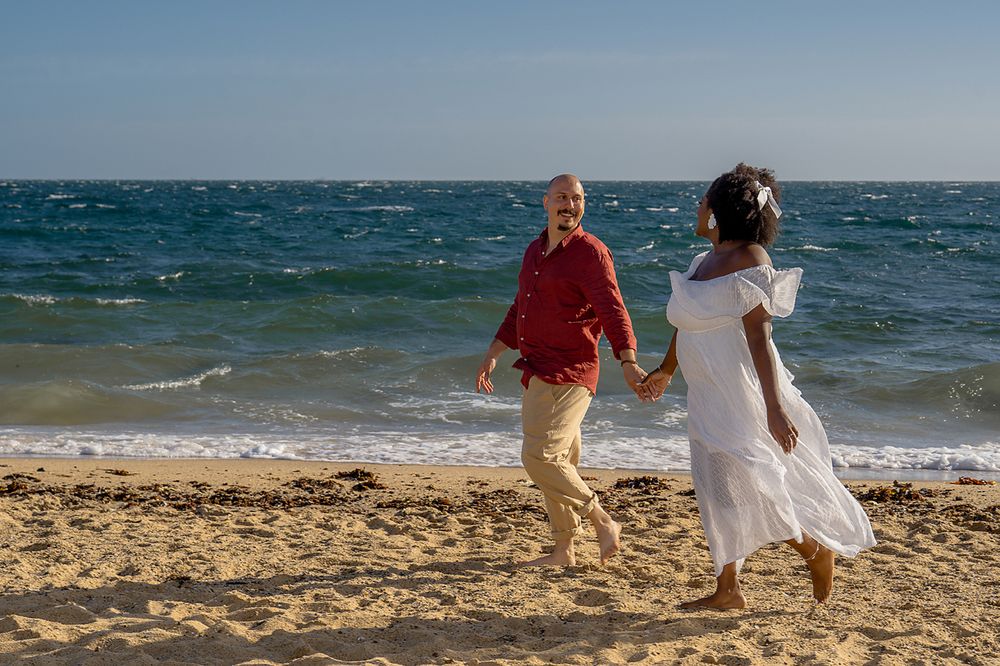 Two people stroll together on a sandy beach with turquoise ocean waters in the background.
