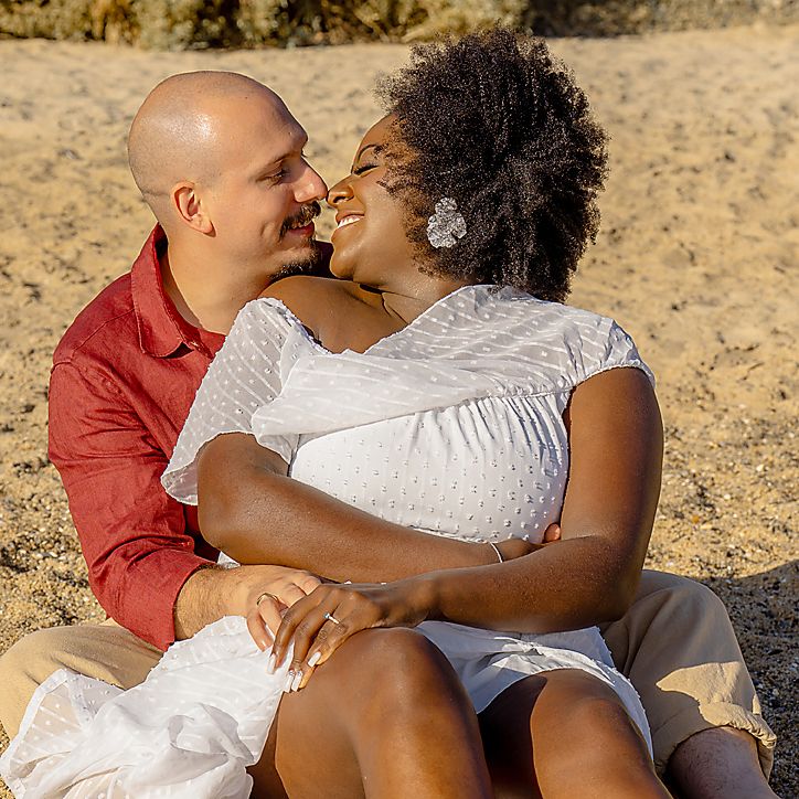 A couple shares a romantic moment together on a sandy beach during golden hour sunset.