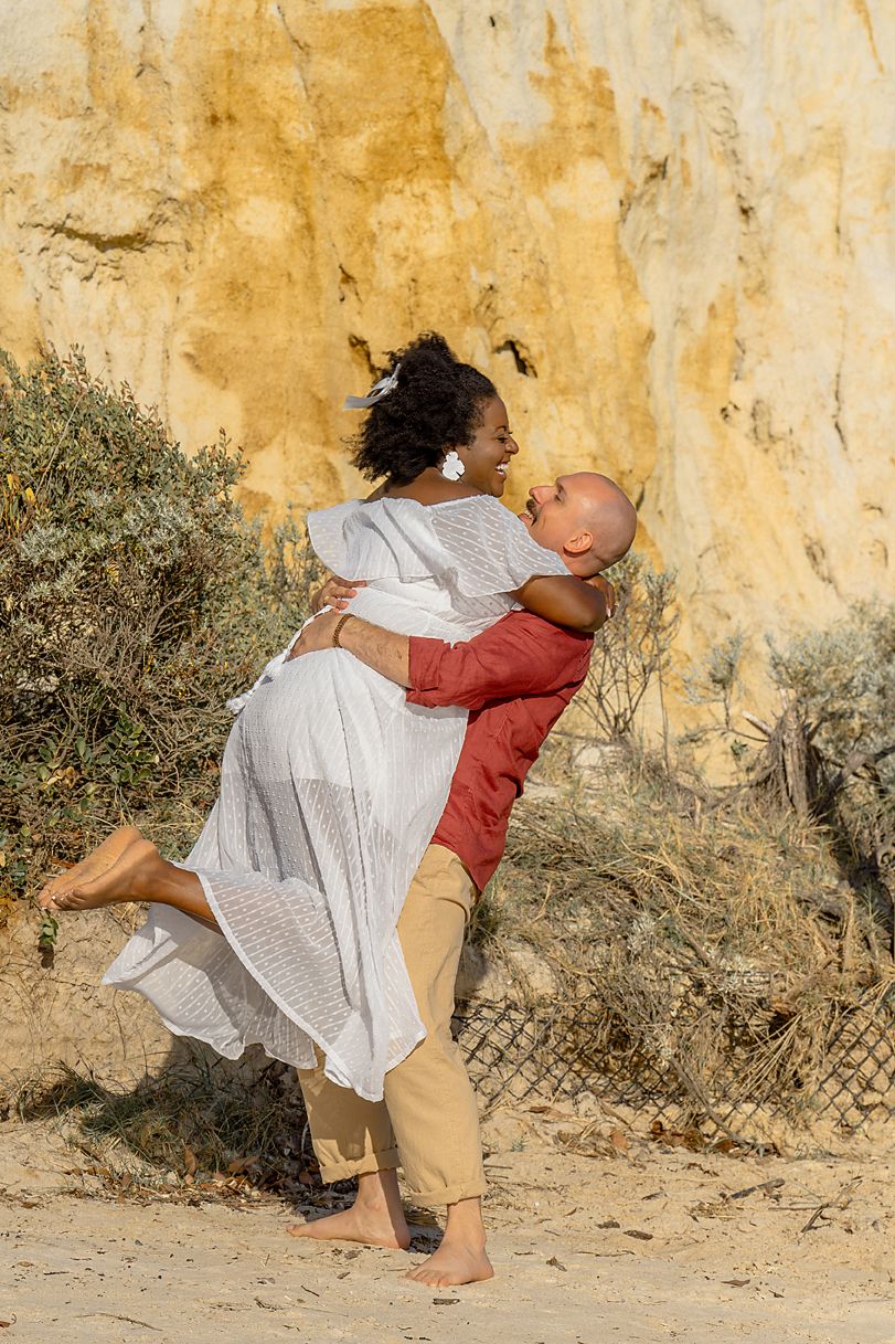 Two dancers in white and red perform an intimate contemporary dance duet against a weathered yellow wall.
