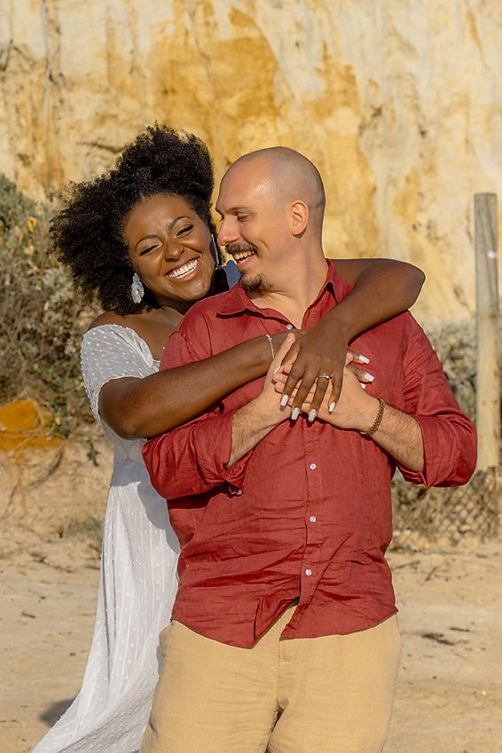 A couple in matching red and khaki outfits share a joyful embrace against a weathered yellow wall.