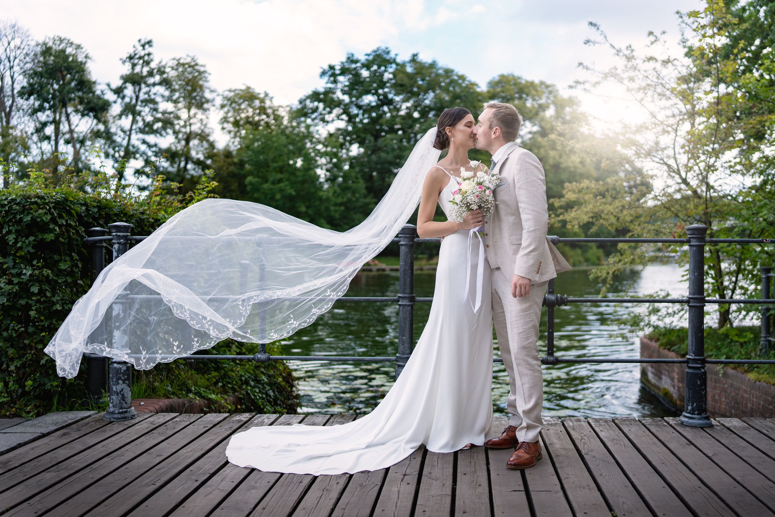Hochzeitsfotograf Berlin  Brandenburg  - Bräutigam küsst die Braut, Schleier fliegt im Sonnenuntergang. Best Hochzeitsfotograf Berlin