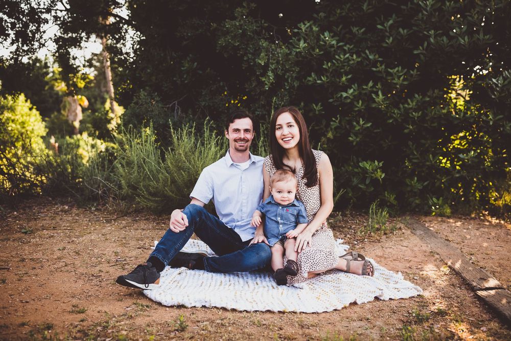 A series of outdoor family portraits taken at sunset in a wooded area with natural lighting and a white blanket on the ground.