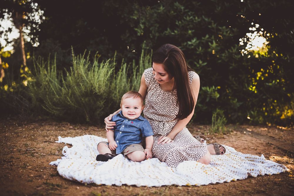 A tender outdoor family moment captured during golden hour on a white blanket surrounded by greenery.