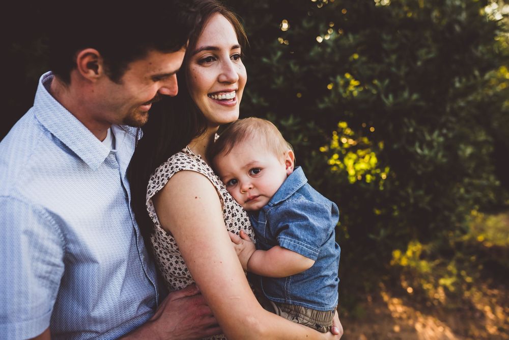 Family in coordinated blue and white outfits embraces during golden hour outdoor photoshoot.