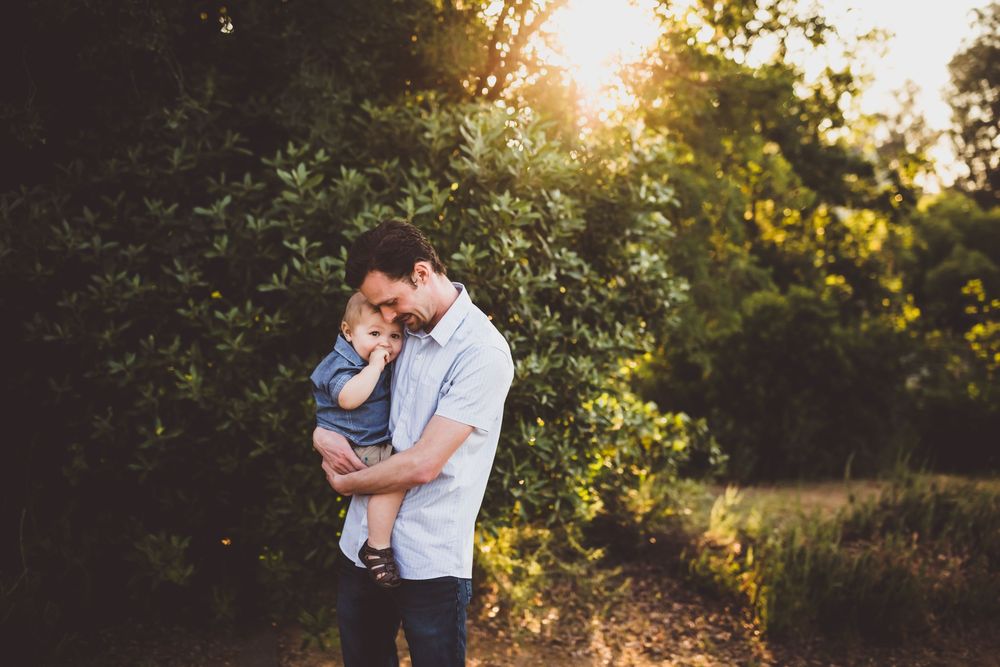 Family portrait session in a sun-dappled wooded area during golden hour.