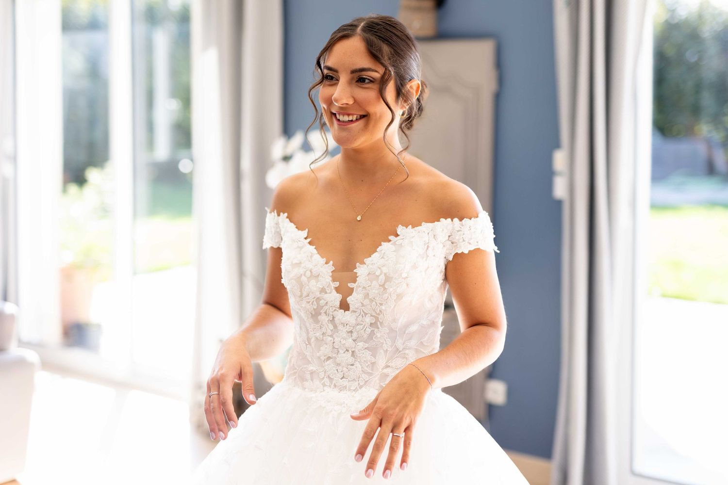 Une personne rayonnante portant une élégante robe de mariée à épaules dénudées avec des détails en dentelle et une jupe ample en tulle.