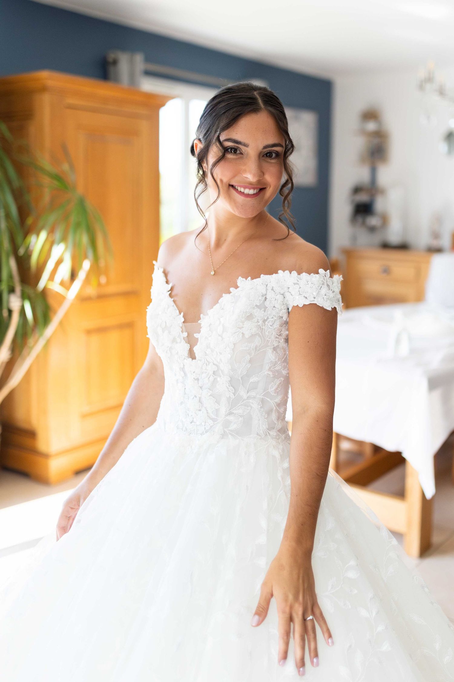 Magnifique robe de mariée avec corsage en dentelle à épaules dénudées et jupe ample en tulle présentée dans une pièce à la lumière naturelle