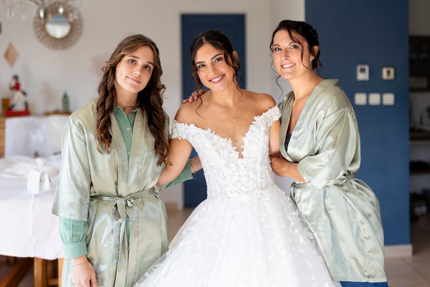 Trois personnes vêtues de robes vert sauge assorties posent avec une mariée portant une robe de mariée en dentelle blanche ornée.
