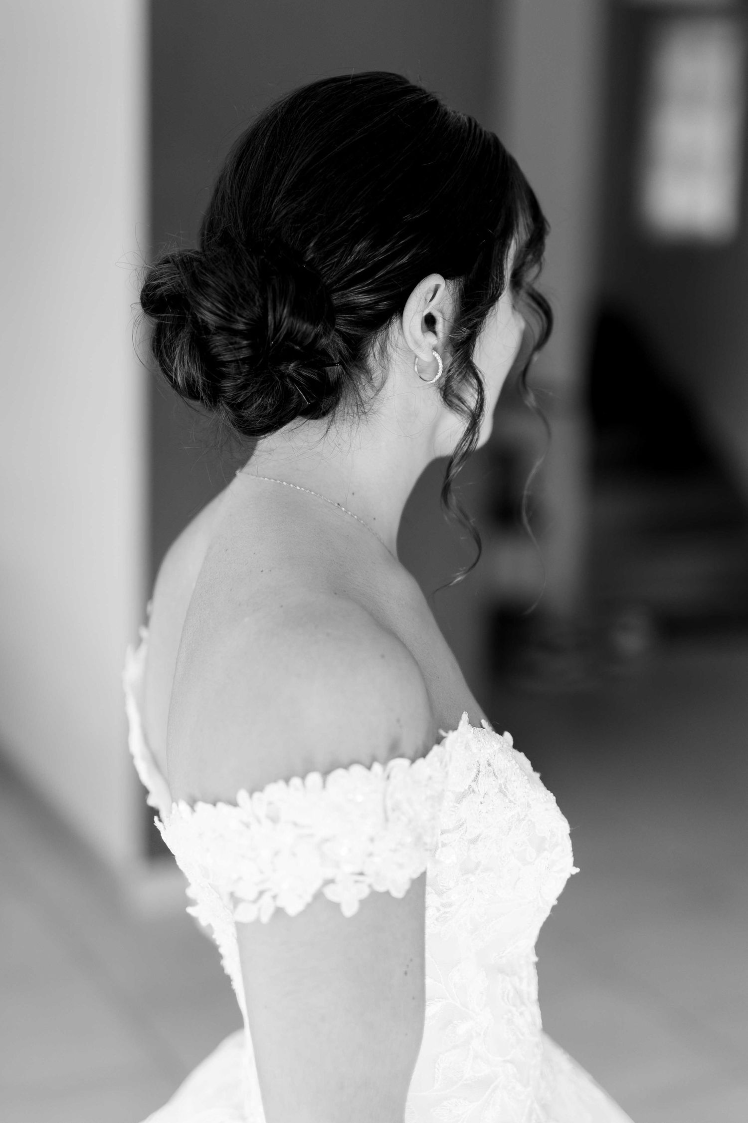 Photo en noir et blanc de la mariée vêtue d'une robe de mariée en dentelle à épaules dénudées, les cheveux coiffés d'un élégant chignon, mon