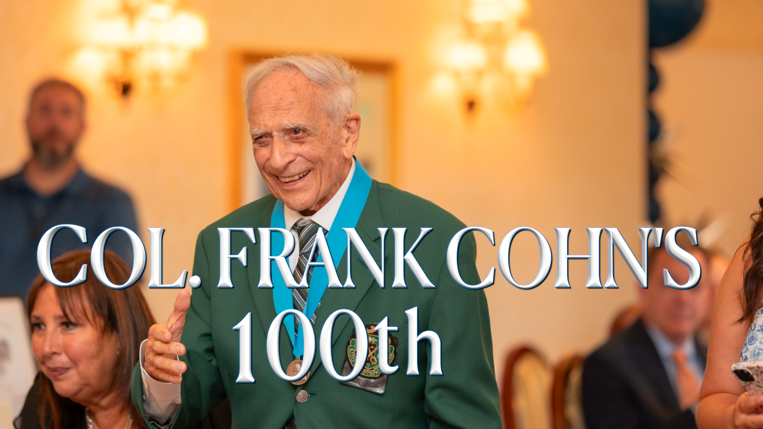 A celebration banner reads 'Col. Frank Cohn's 100th' at an elegant party with warm lighting and wall sconces.