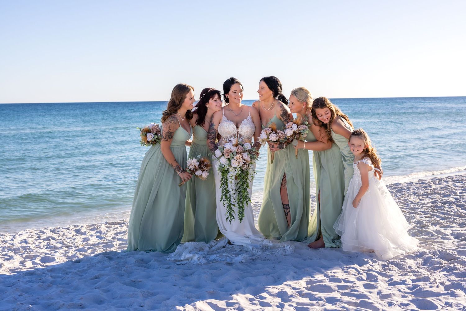 Wedding party celebrating on a white sandy beach with ocean waves in the background.
